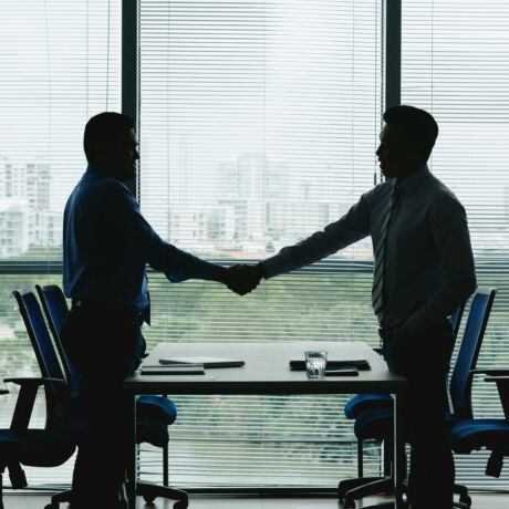 Silhouettes of businessmen shaking hands after signing documents